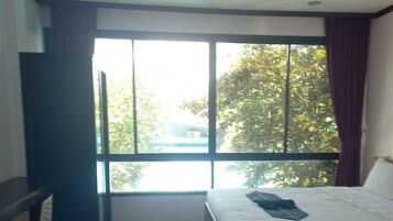 Un dormitorio con una cama, una ventana con cortinas y vistas a árboles.