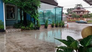 Un edificio con fachada de vidrio, rodeado de plantas en macetas y suelo mojado, lo que sugiere lluvia reciente.