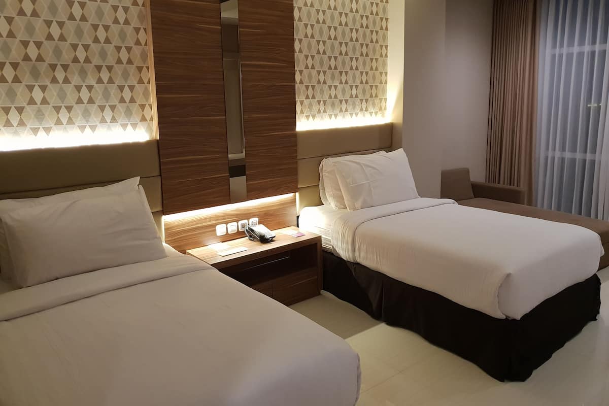 A hotel room with two beds, a nightstand, a desk, and a chair.