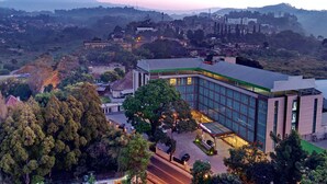 A modern hotel with a glass facade, surrounded by trees and a hilly landscape. - Novena Hotel (Lembang)