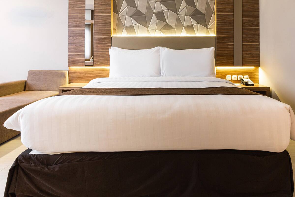A hotel room with a large bed, a bedside table with a phone, and a wall-mounted light fixture.