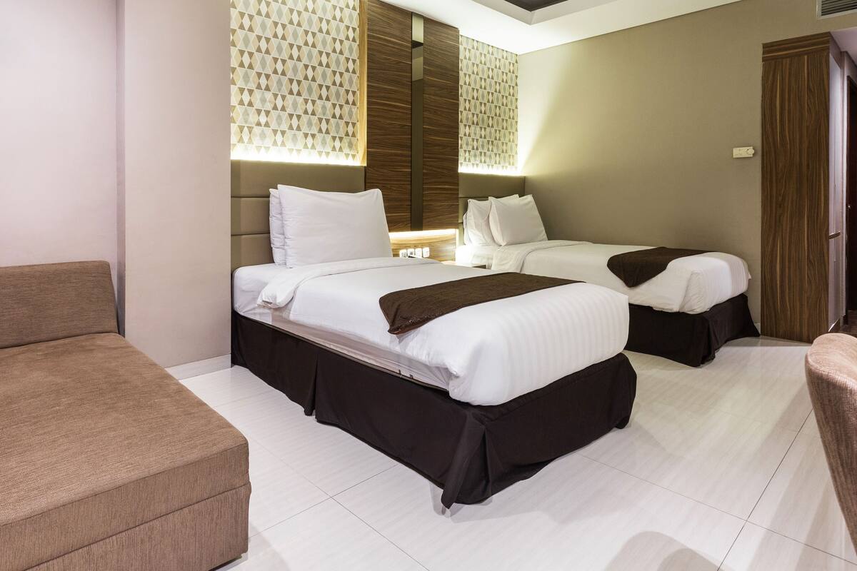 A hotel room with two beds, a sofa, and a small table.