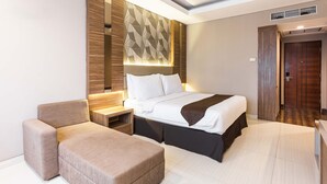 A modern hotel room with a large bed, a bedside table, a chair, and a wardrobe. - Novena Hotel (Lembang)