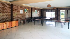 A spacious indoor area with a brick wall, tiled floor, and multiple tables and chairs. - Terra Villa Resort (Chok Chai)