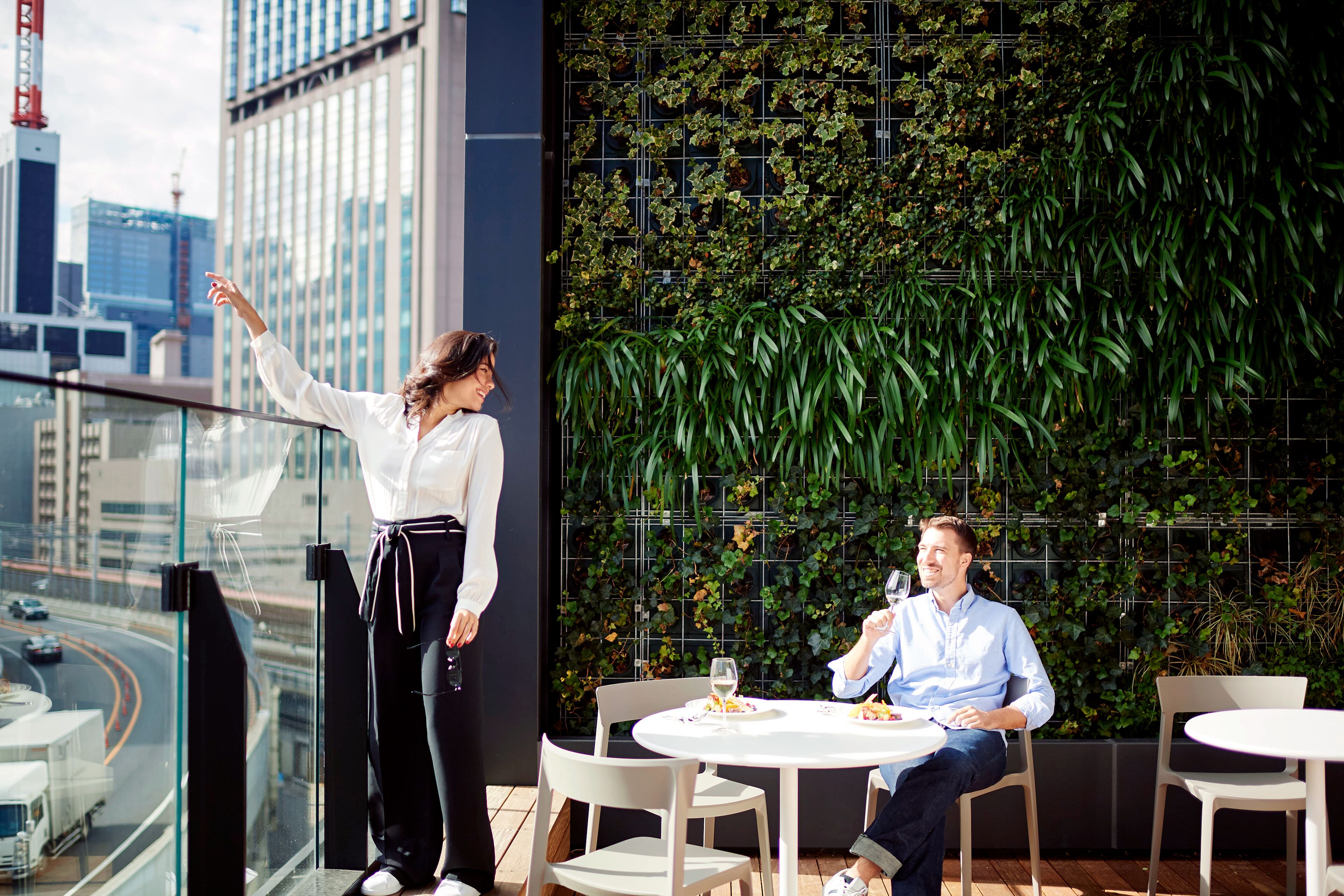 Un homme et une femme sont assis à une table, devant une vue sur la ville et un mur végétal.