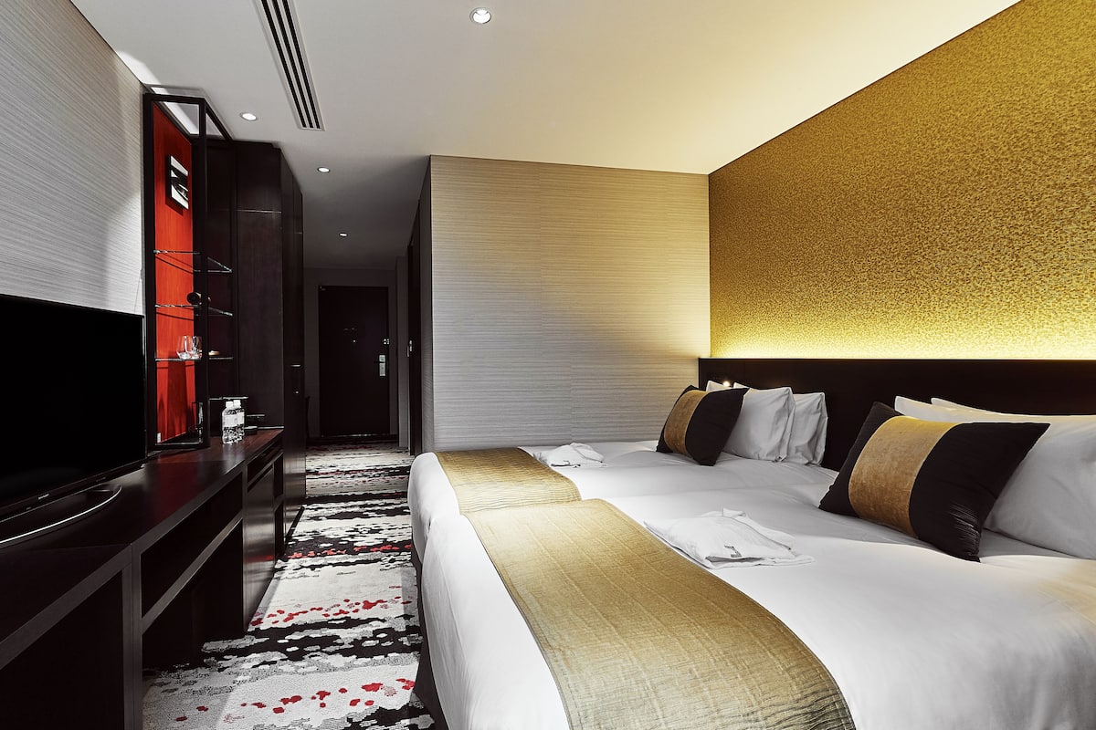 A hotel room with a large bed, a TV, a desk, and a red accent wall.