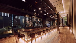 A modern bar area with a long counter, multiple stools, and a view of the city through large windows. - The Gate Hotel Tokyo By HULIC (Tokyo)