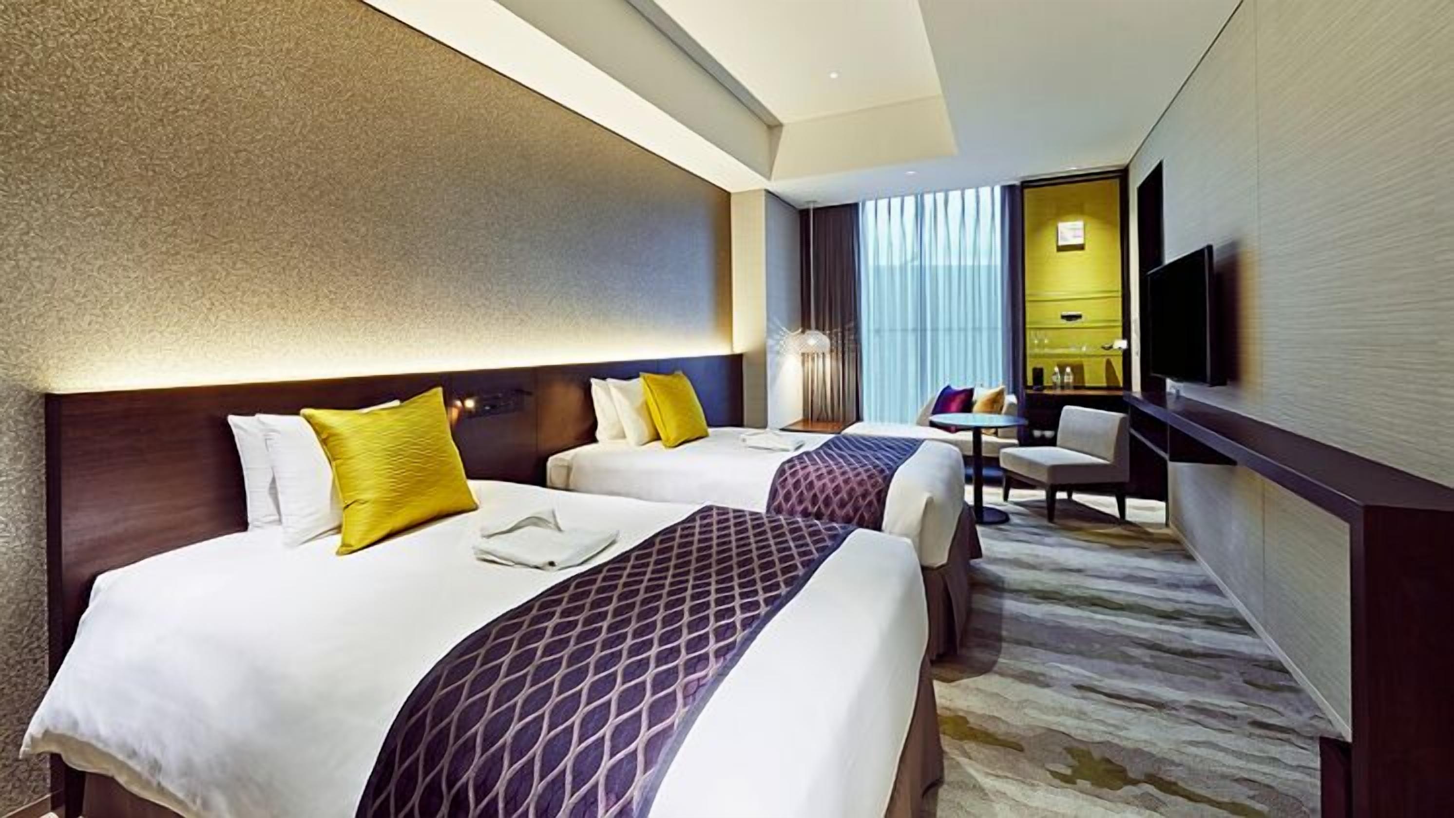 Ein Hotelzimmer mit zwei Betten, einem Schreibtisch, einem Stuhl und einem Fernseher.