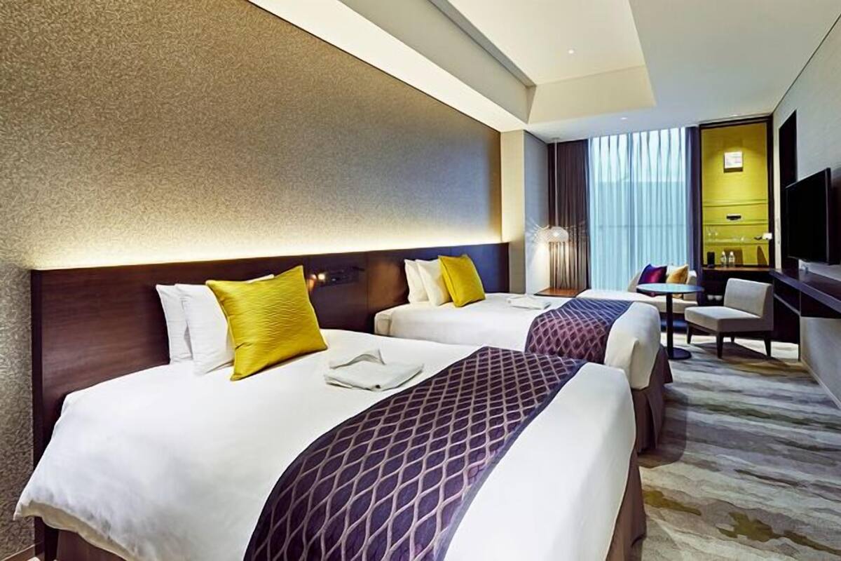 A hotel room with two beds, a desk, a chair, and a television.