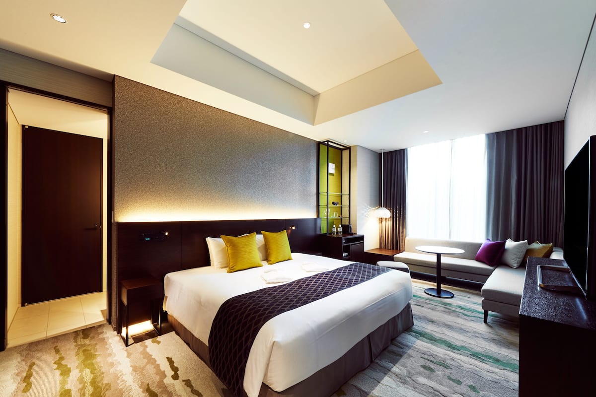 A modern hotel room with a large bed, a desk, a sofa, and a TV.