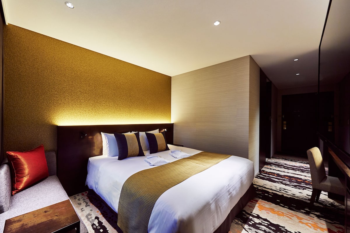 A modern hotel room with a large bed, a desk, and a chair.