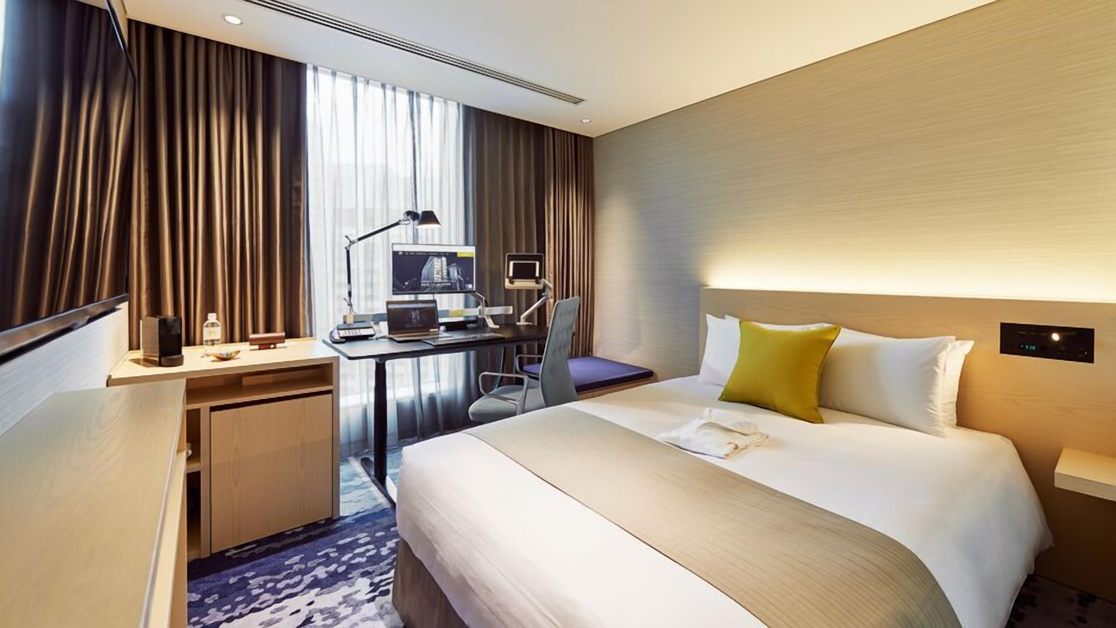 Ein Hotelzimmer mit Bett, Schreibtisch, Computer und Vorhängen.