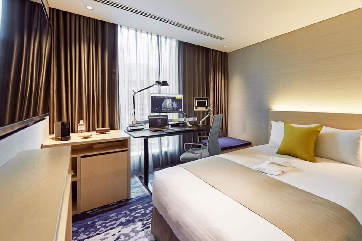 A hotel room with a bed, desk, computer, and curtains.