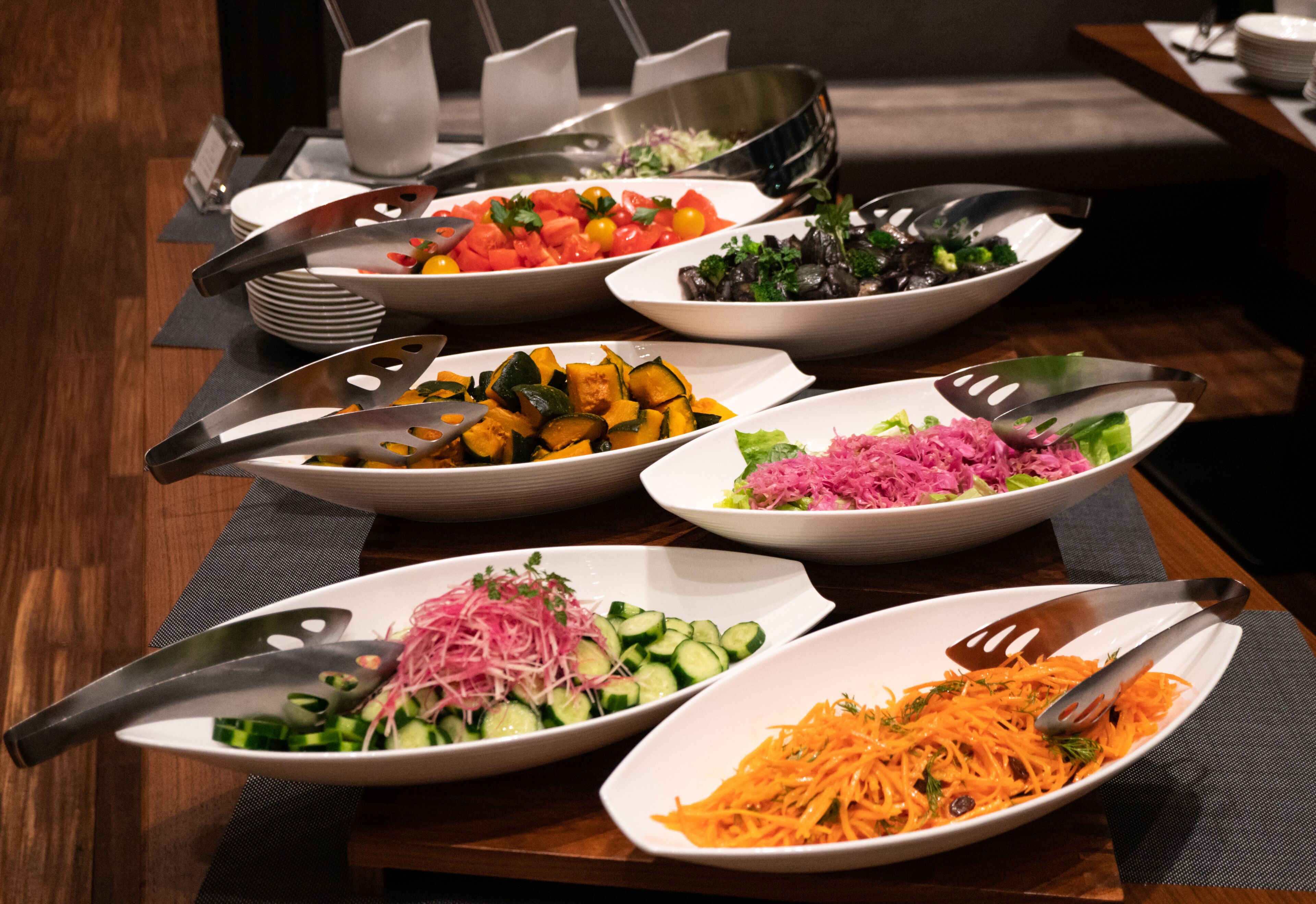 Une table de buffet proposant divers plats, notamment des salades et des légumes, disposés sur une table en bois recouverte de sets de table noirs.