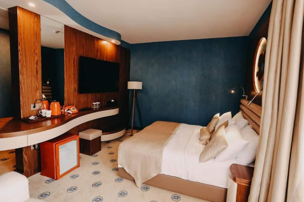 Une chambre d’hôtel avec un grand lit, une coiffeuse en bois avec un miroir, une télévision à écran plat et un petit coin salon.