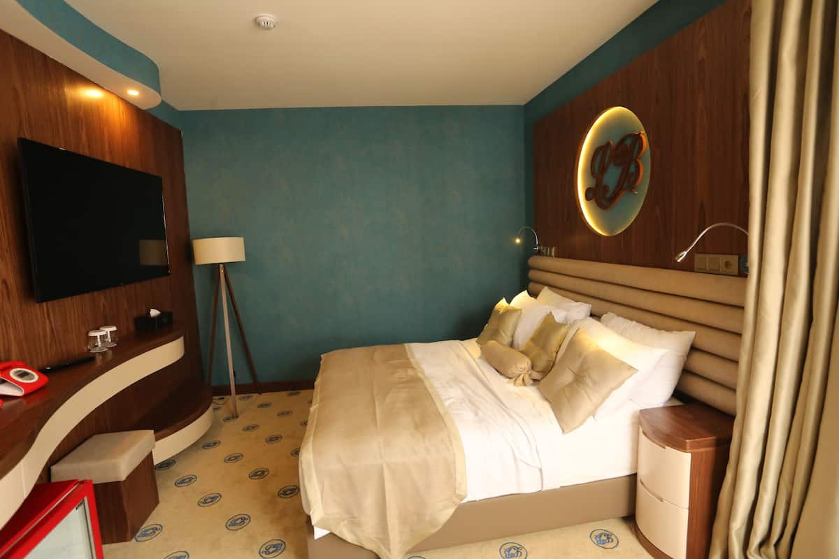 Une chambre d’hôtel avec un grand lit, un téléviseur fixé au mur, une table de chevet et une lampe.