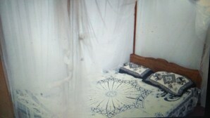 A room with a bed covered by a sheer white curtain, a patterned bedspread, and a wooden headboard. - White House (Unawatuna)