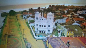An aerial view of a coastal town with a prominent white building with a central tower, surrounded by smaller houses and a beach area. - White House (Unawatuna)