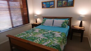 A bedroom with a bed, two nightstands, a window with blinds, and wall art. - Palm Lakeside - Bowen, Whitsundays Wifi Netflix Private Cool Luxury (Bowen)