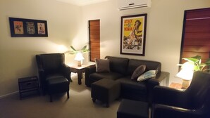 A living room with a sofa, two armchairs, a small table with a lamp, and a poster on the wall. - Palm Lakeside - Bowen, Whitsundays Wifi Netflix Private Cool Luxury (Bowen)