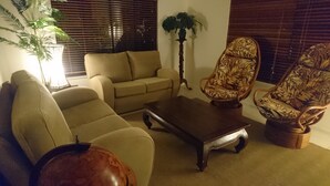 A living room with a beige sofa, a wooden coffee table, and two wicker armchairs with a leaf pattern. - Palm Lakeside - Bowen, Whitsundays Wifi Netflix Private Cool Luxury (Bowen)