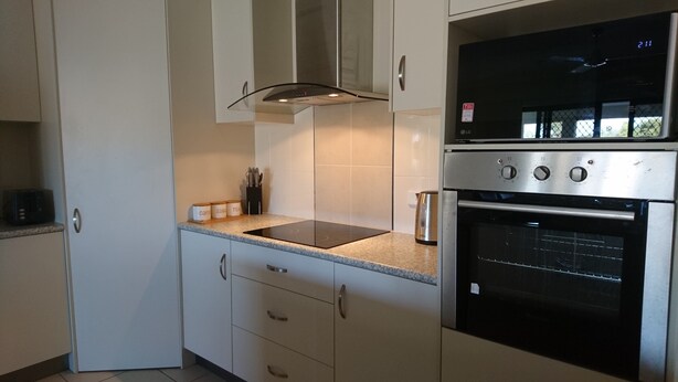 A modern kitchen with white cabinets, a built-in oven, and a countertop with a kettle. - Palm Lakeside - Bowen, Whitsundays Wifi Netflix Private Cool Luxury (Bowen)