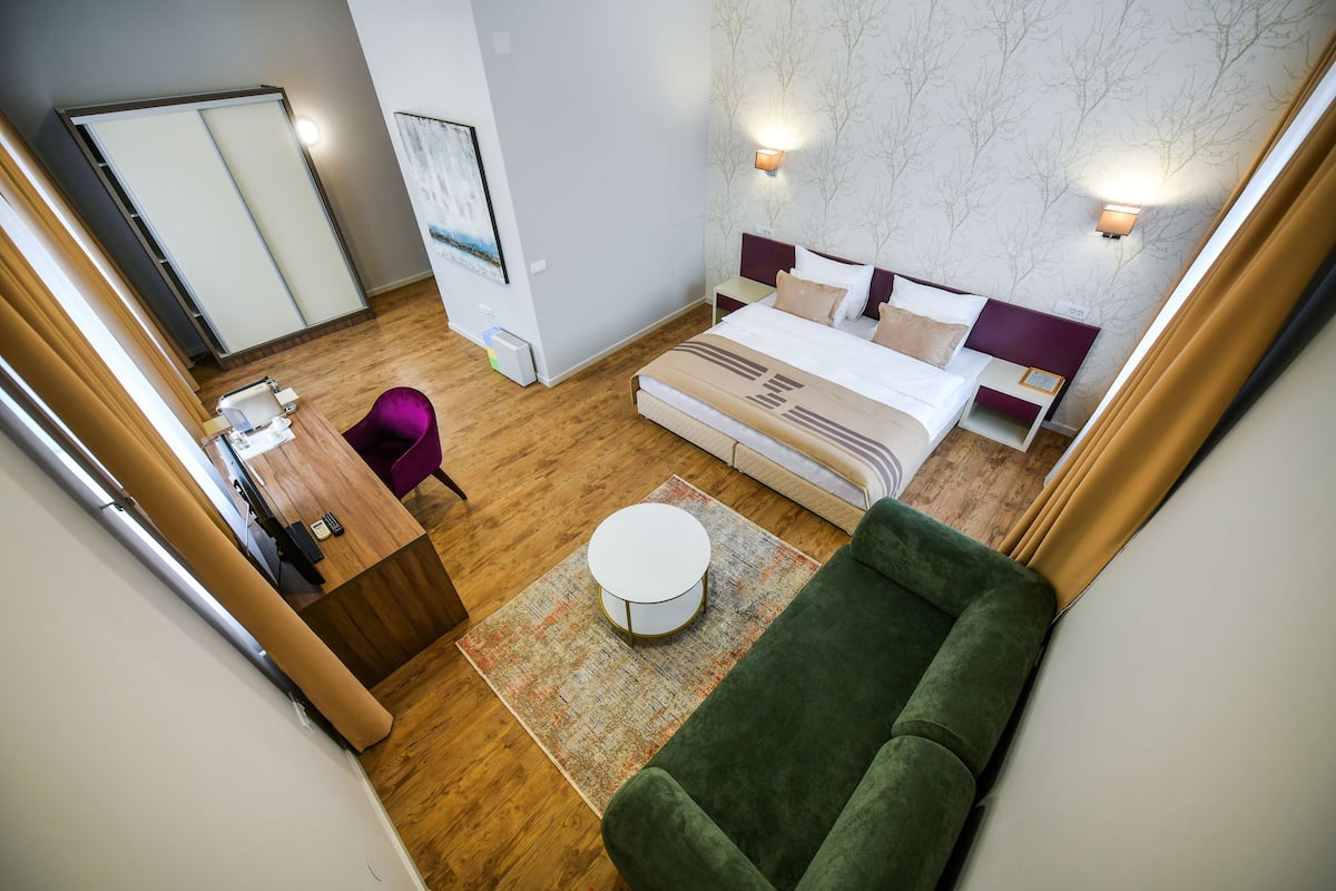 A hotel room with a bed, a green sofa, a small round table, and a desk with a chair.