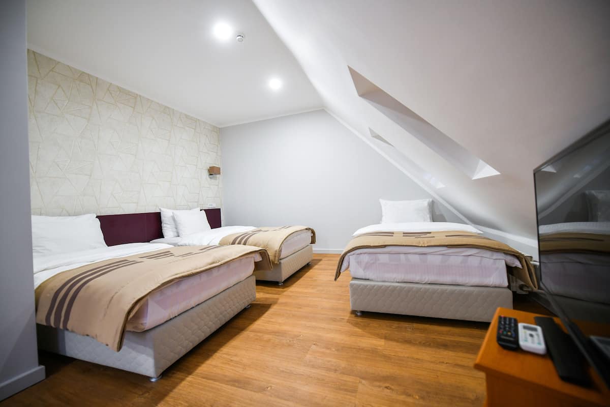 A modern hotel room with two beds, wooden flooring, a stone-patterned wall, and a television on a wooden side table.