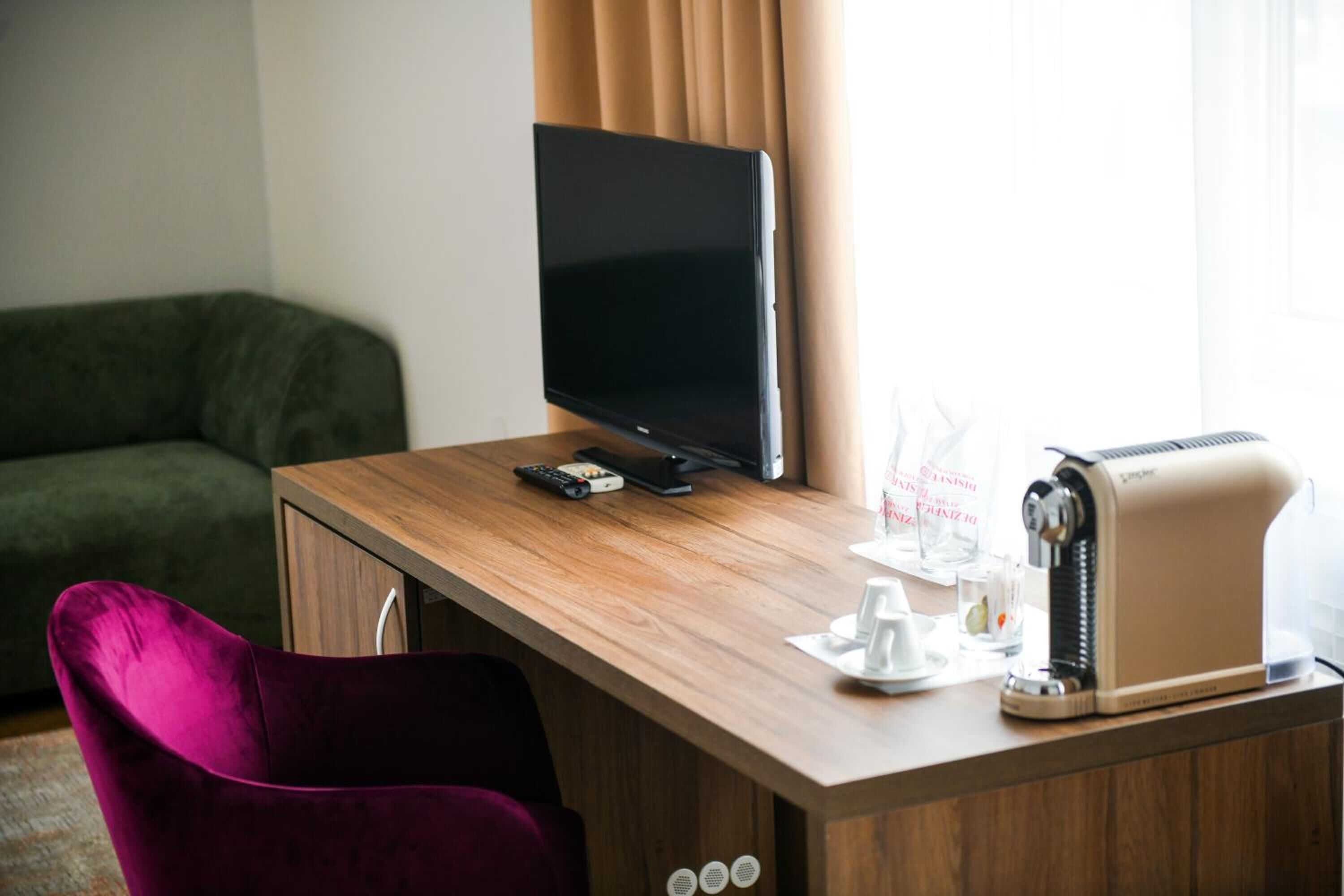 Una habitación de hotel con un escritorio de madera, un televisor de pantalla plana, un tostador y una silla morada.