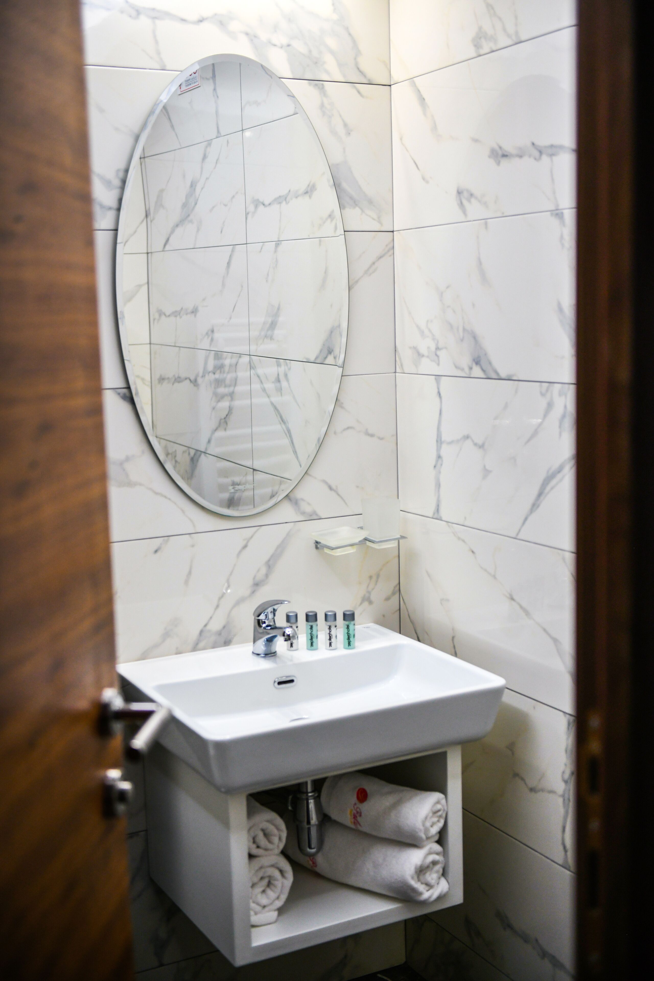 Un bagno con un lavandino bianco, uno specchio e un portascopevoli.
