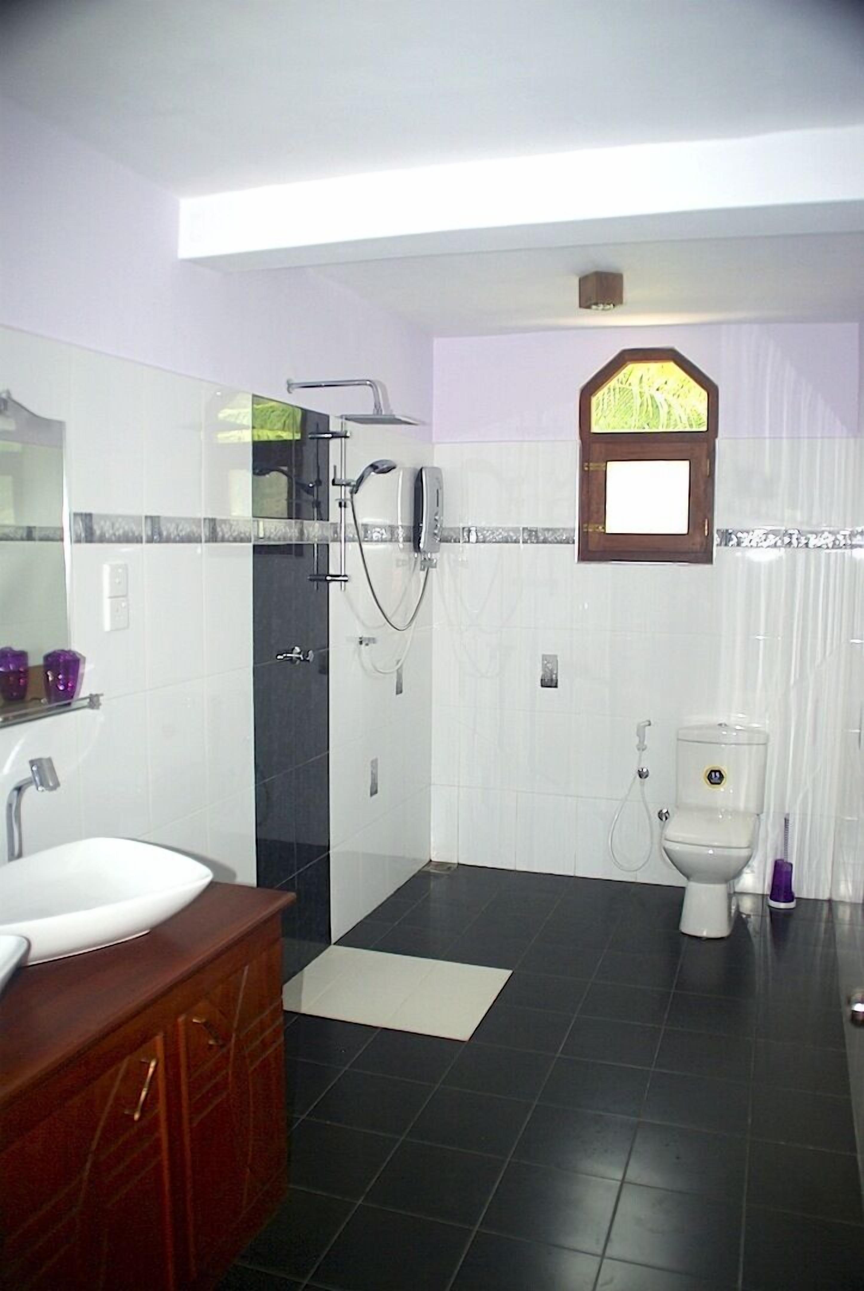 Une salle de bain avec un lavabo blanc, des carreaux foncés, une douche et des toilettes.