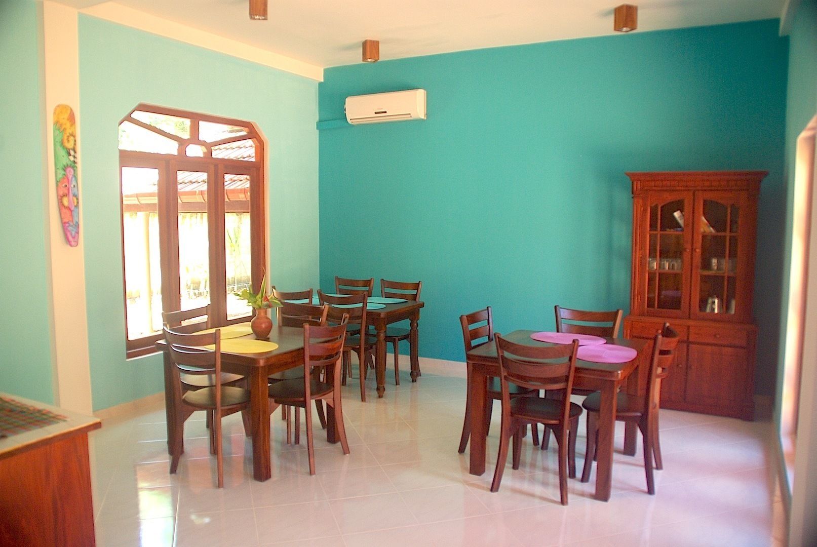 A dining area with wooden tables and chairs, a cabinet, and a window with a view.