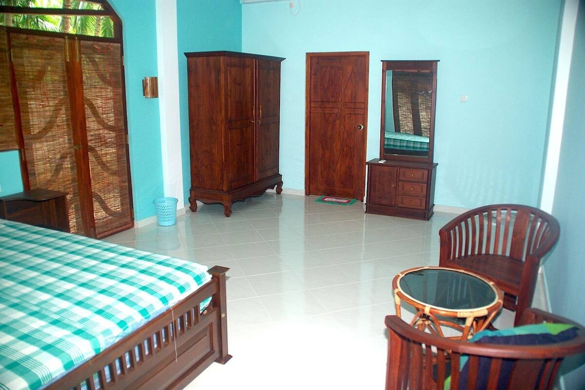 A bedroom with a bed, a wooden wardrobe, a mirror, a chair, and a small table.