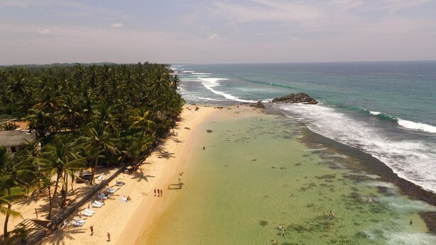 A beach with clear turquoise waters, a sandy shore, and a line of palm trees. - King Coconut Lodge (Koggala)
