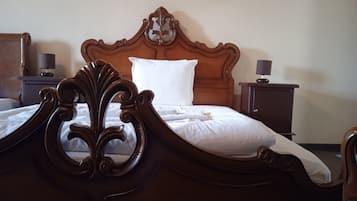 Una cama bien tendida con cabecera de madera, dos mesitas de noche con lámparas y un pequeño armario.