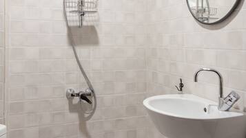 A bathroom with a toilet, a sink, a shower with a handheld showerhead, and a mirror with an ornate frame.