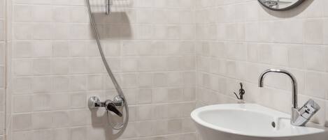 A bathroom with a toilet, a sink, a shower with a handheld showerhead, and a mirror with an ornate frame.