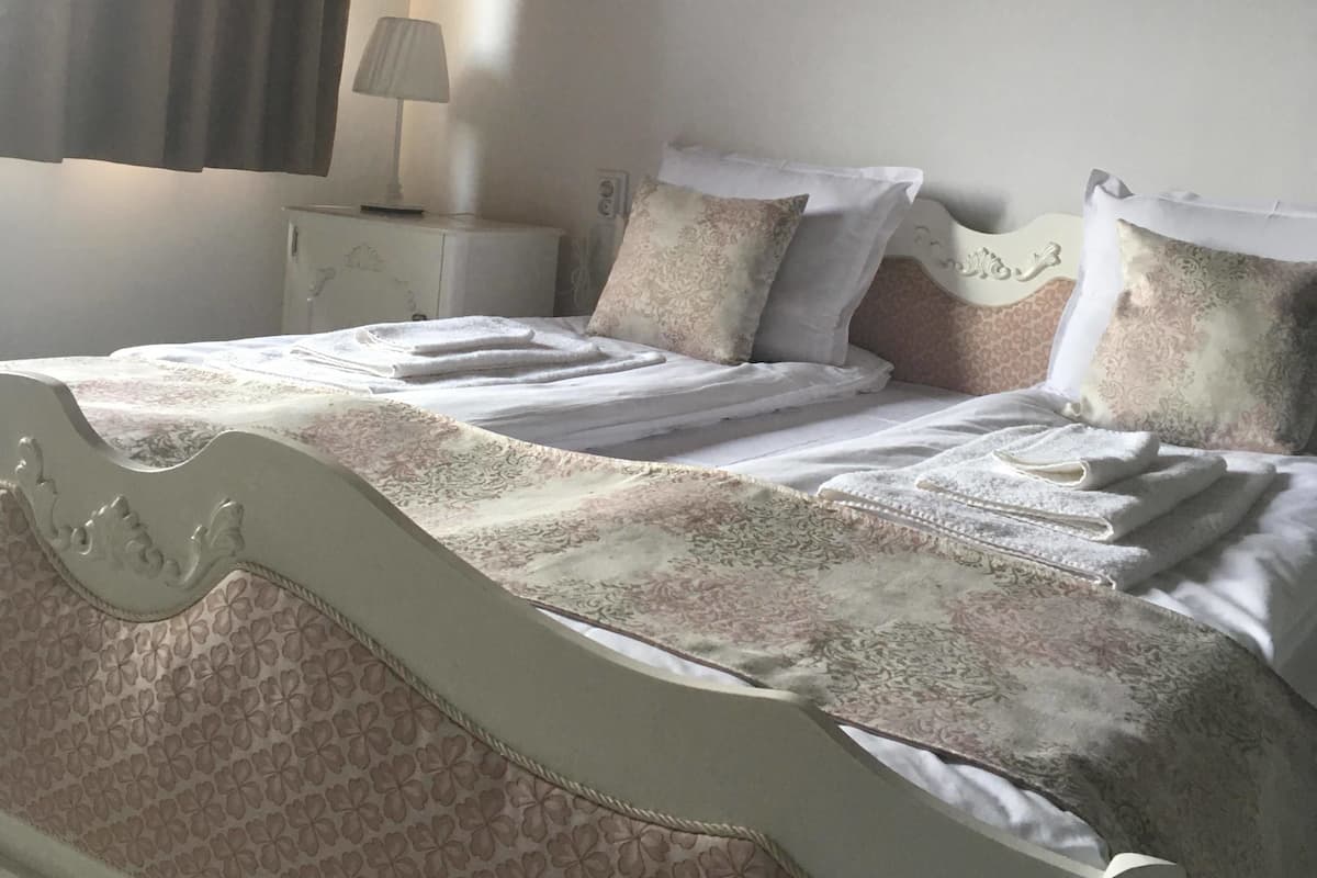 Een netjes opgemaakt bed met een bedsprei met een patroon, een nachtkastje met een lamp en een aan de muur hangend schilderij.