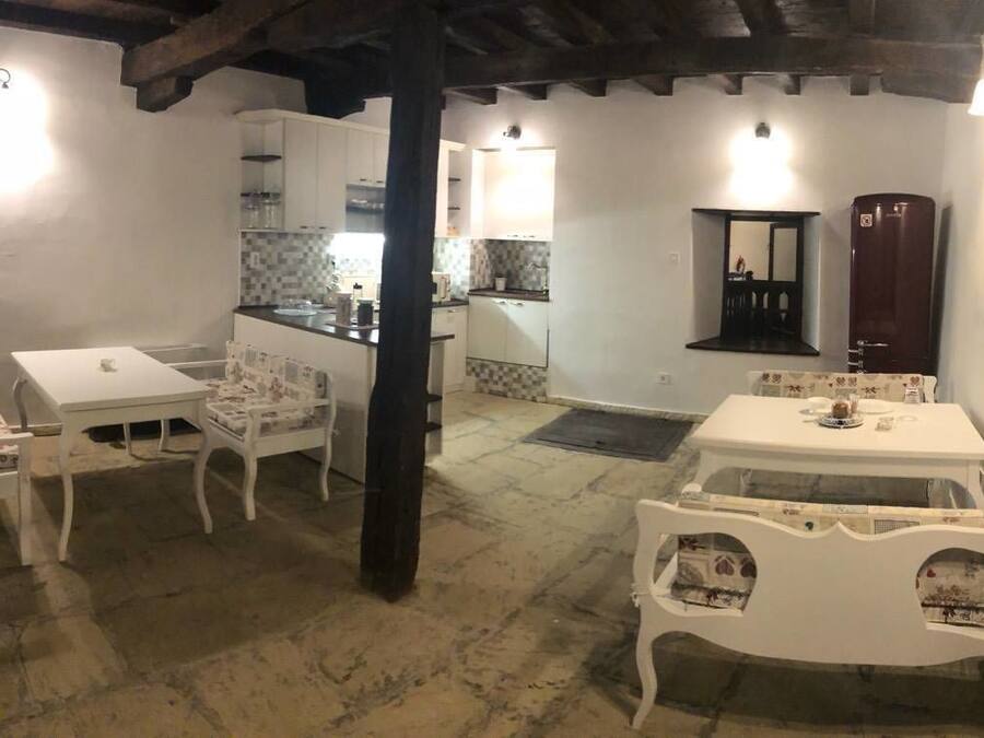 A rustic kitchen with white cabinets, a wooden ceiling, and a dining area with white furniture.