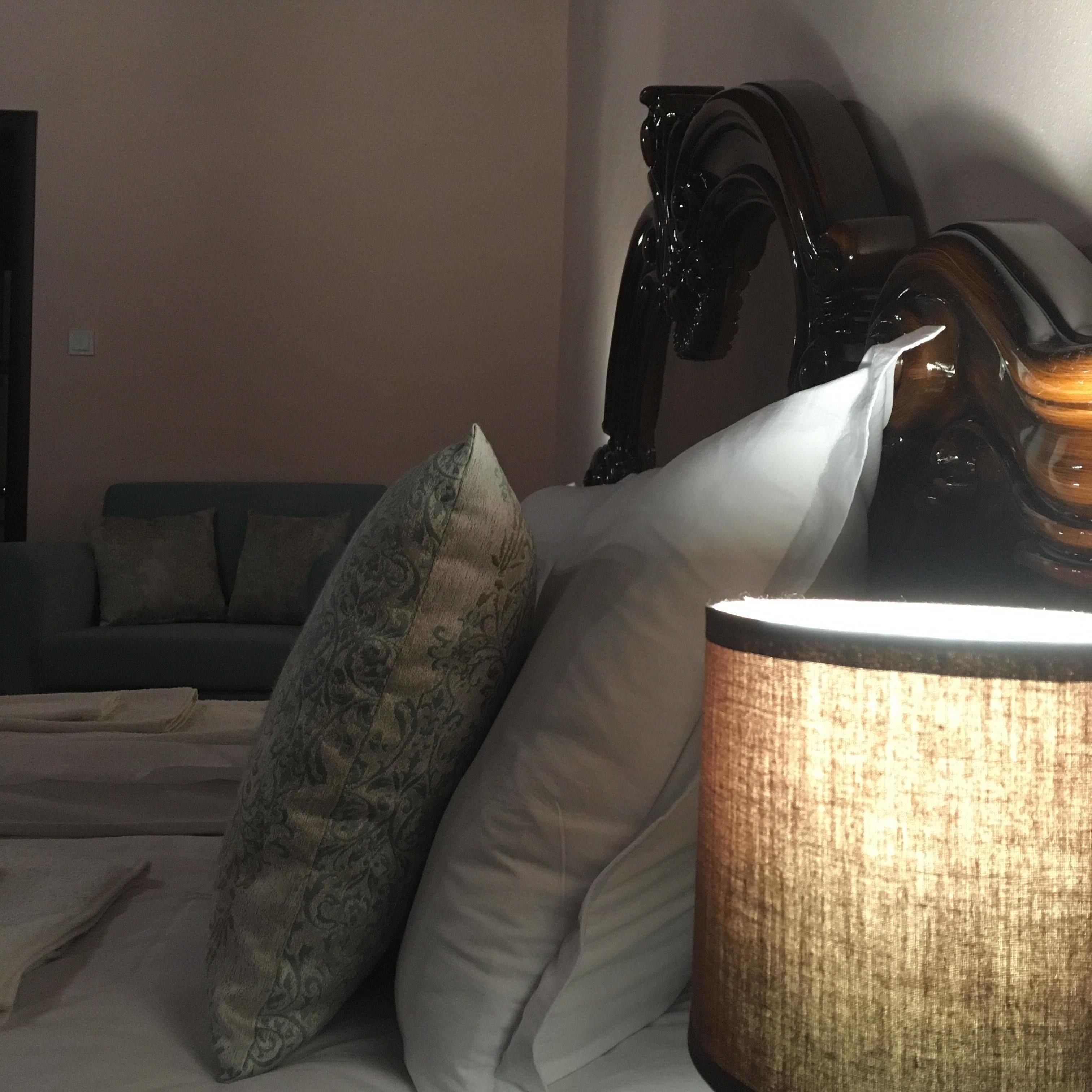 Una habitación de hotel con cama, almohadas, una lámpara y un cabecero de madera.