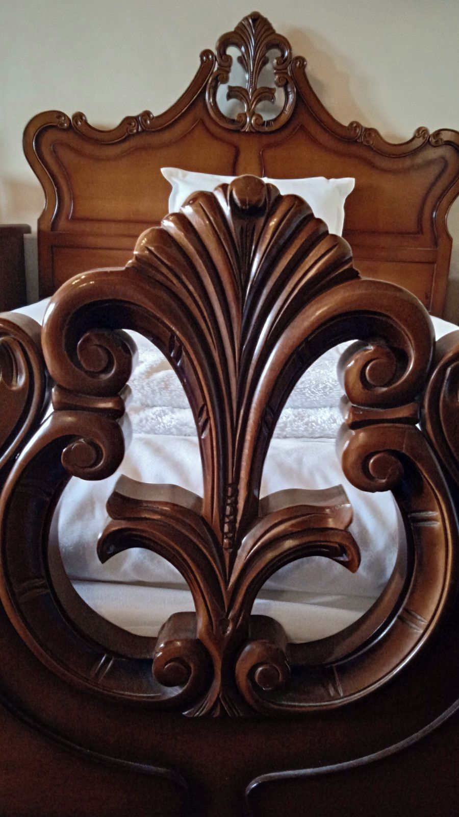 A bed with an ornate wooden headboard and a white pillow.