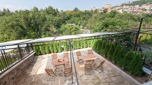A stone patio with outdoor furniture, a view of a hillside with greenery and a distant building.