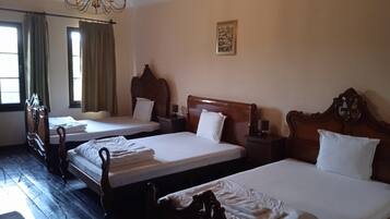 A hotel room with three wooden beds, each with white linens, a wooden headboard, and a bedside table with a lamp.