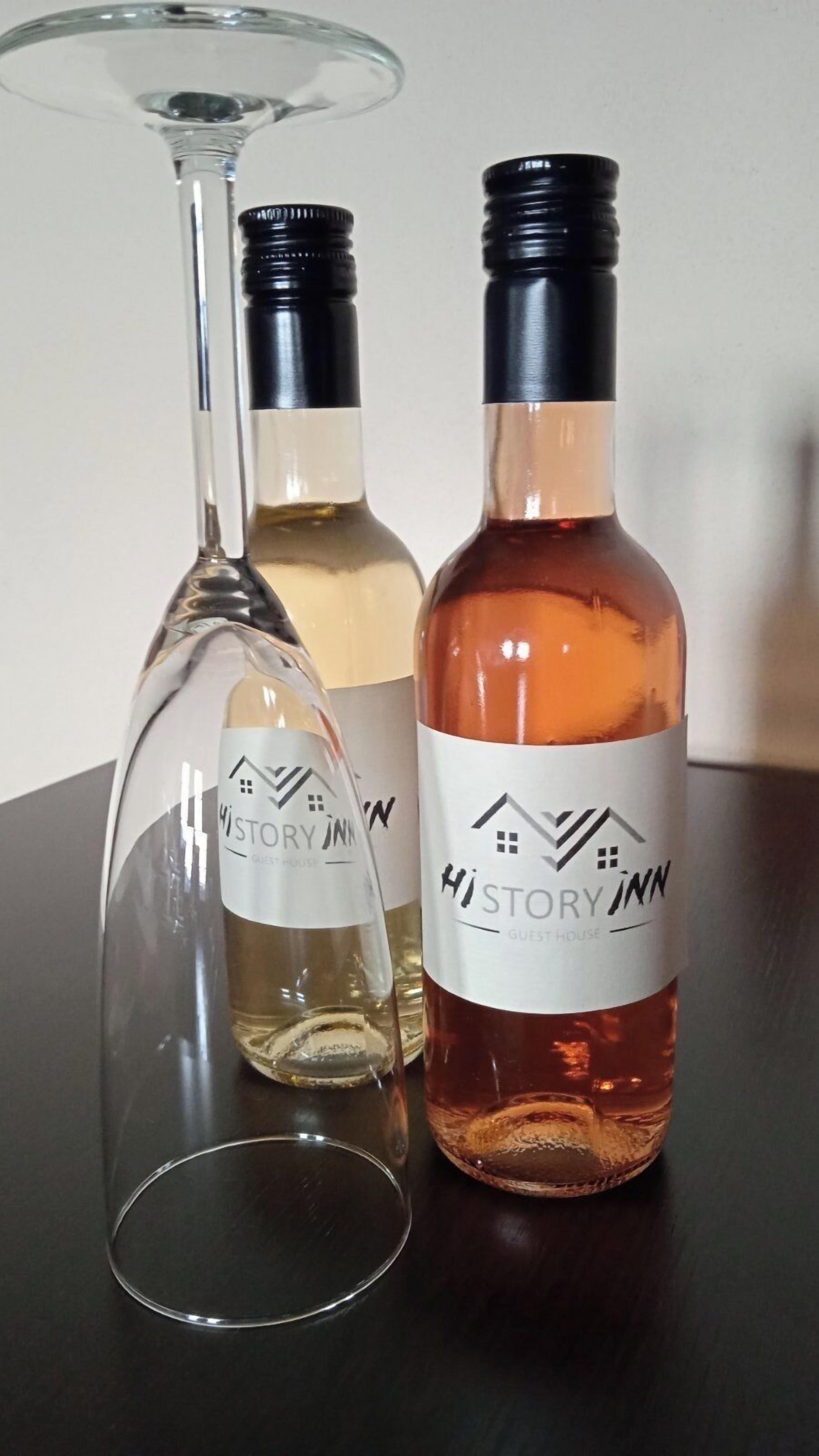 Two bottles of History Inn Guest House wine and a wine glass on a table.