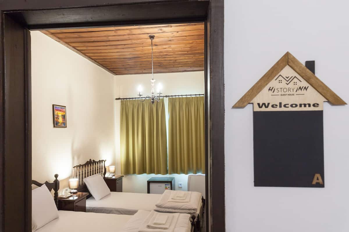 Een hotelkamer met twee bedden, een houten plafond, een kroonluchter, een bureau met een lamp en een 'Welcome'-bord.