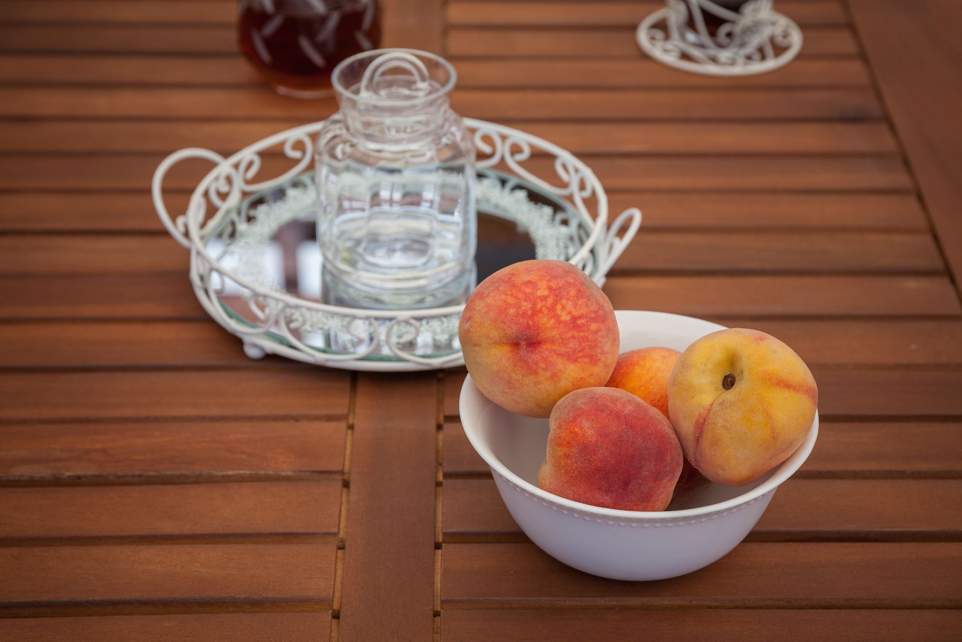 A wooden table with a white bowl containing peaches and a glass pitcher.