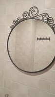 Un espejo redondo con un marco metálico decorativo sobre una pared con azulejos.