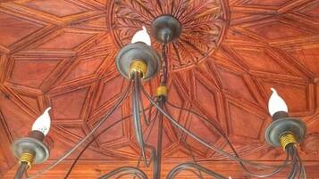 Um candelabro com vários braços e lâmpadas, sobre um teto de madeira ricamente detalhado.