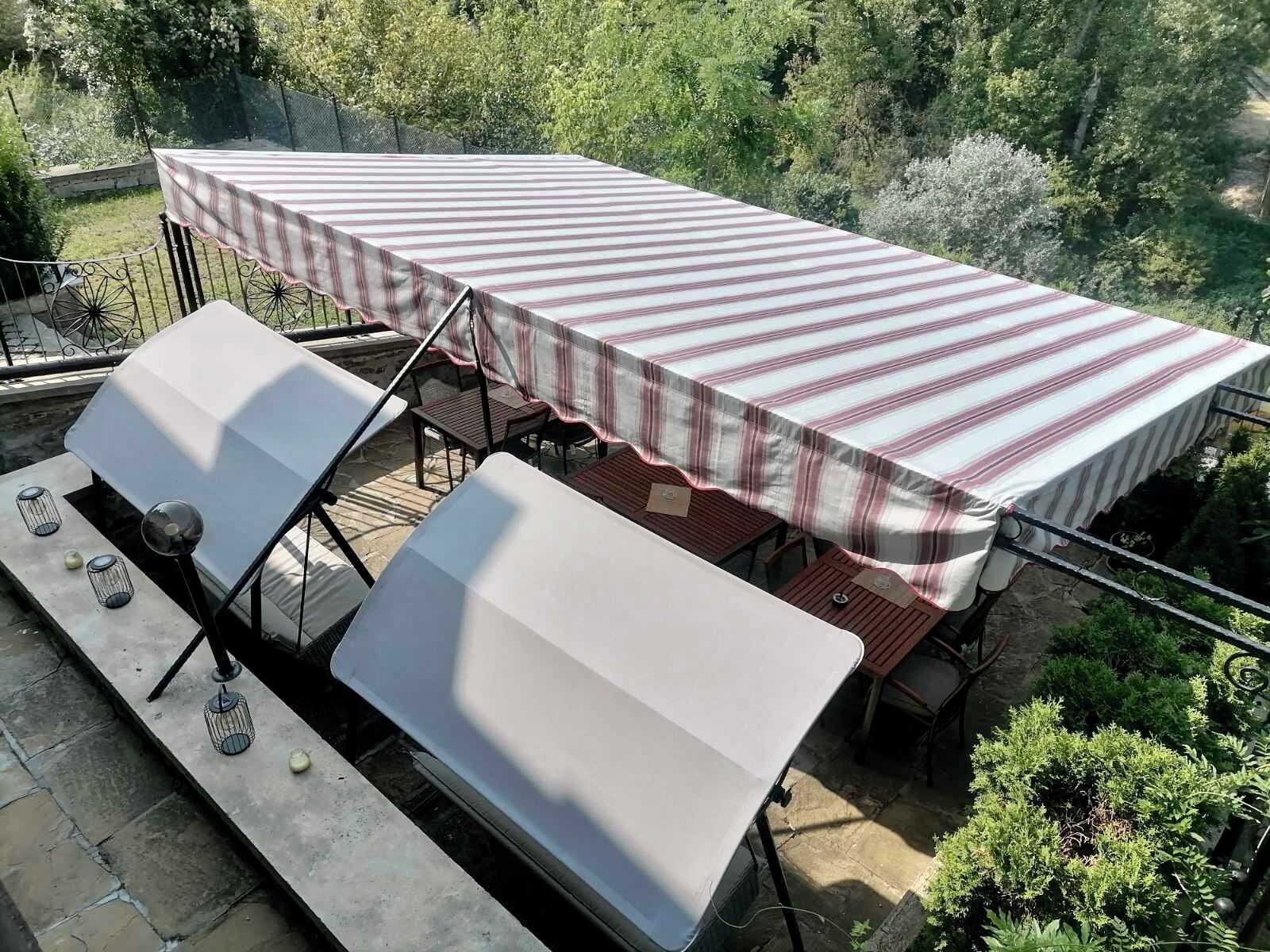 Un patio al aire libre con una mesa cubierta por un mantel a rayas, dos bancos blancos acolchados y una parrilla.