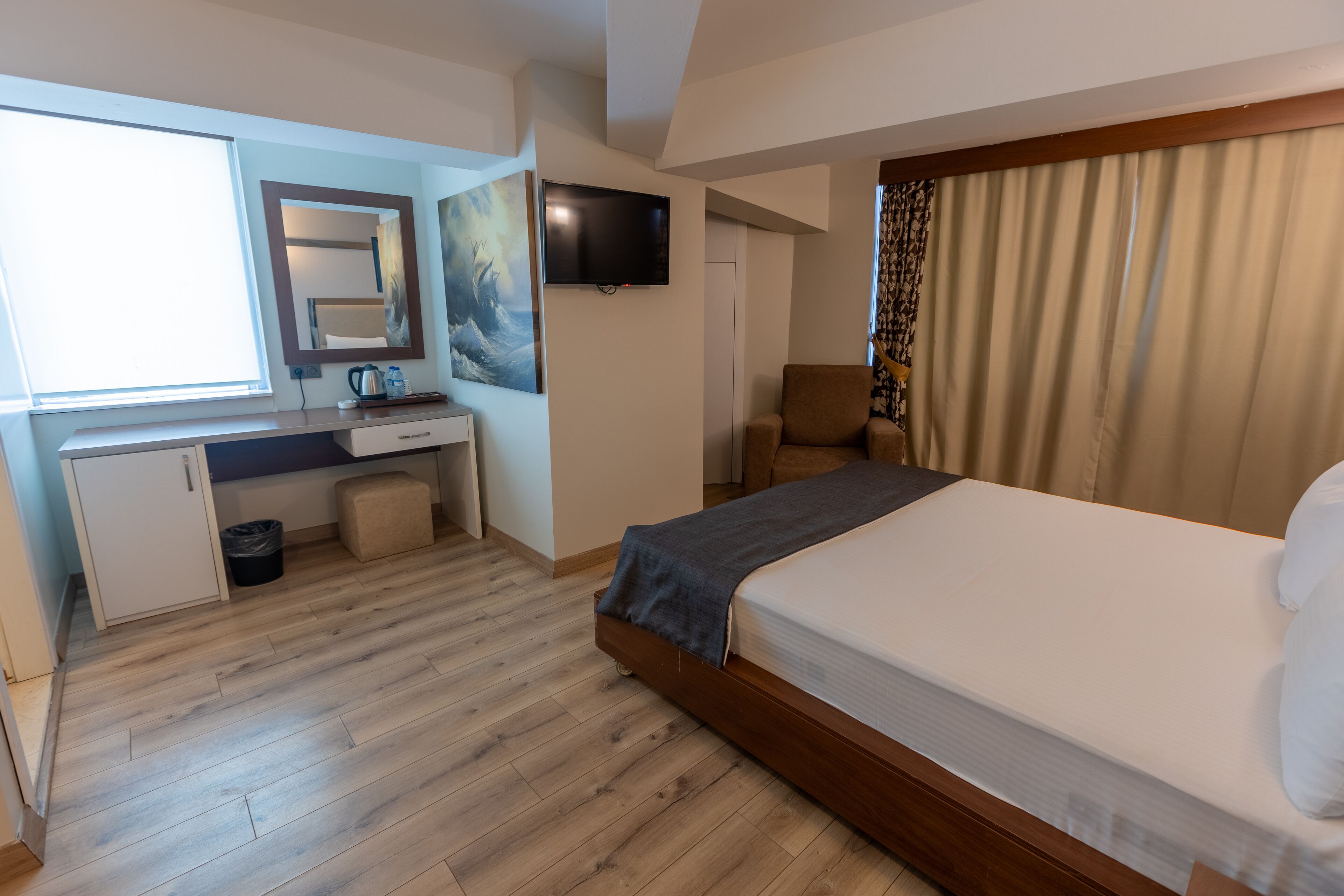 Une chambre d’hôtel avec un lit, un bureau avec un ordinateur, une télévision et une fenêtre avec des rideaux.